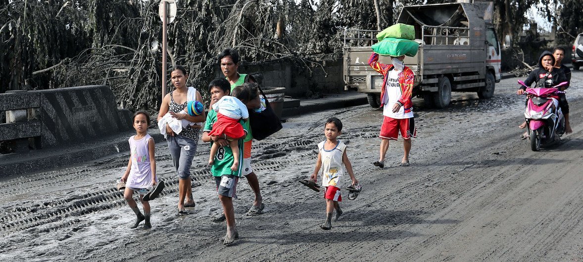 A family affected by the eruption of the Taal volcano in 2020 walks in volcanic ash-covered streets.