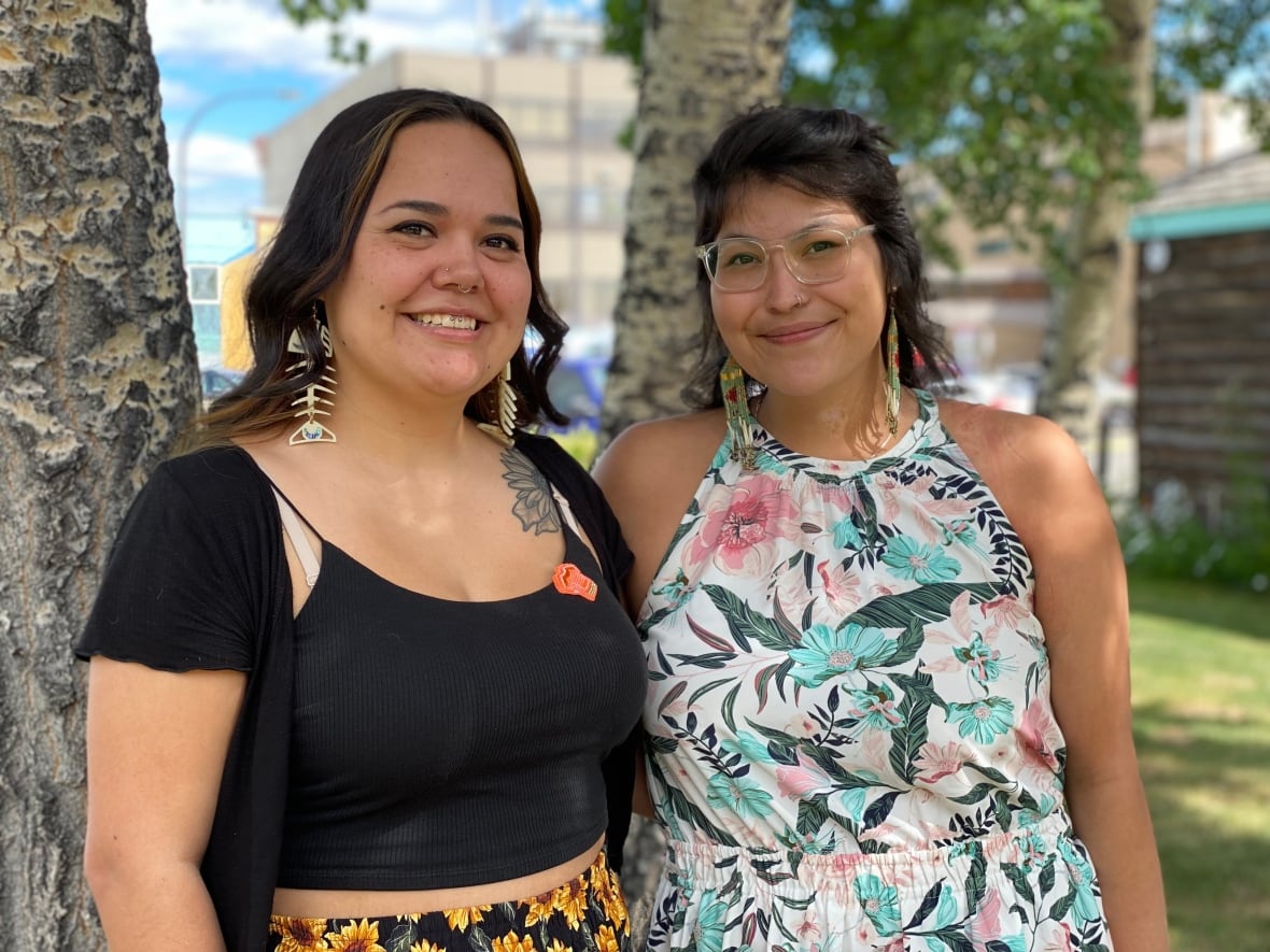 Two smiling young women stand together on a lawn.