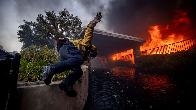 A firefighter jumps over a fence while fighting the Palisades Fire in the Pacific Palisades neighbourhood of Los Angeles, Tuesday, Jan. 7, 2025. (AP Photo/Ethan Swope)