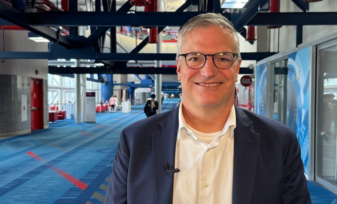 A man in glasses and a blazer poses for a photo inside a hotel conference hallway.