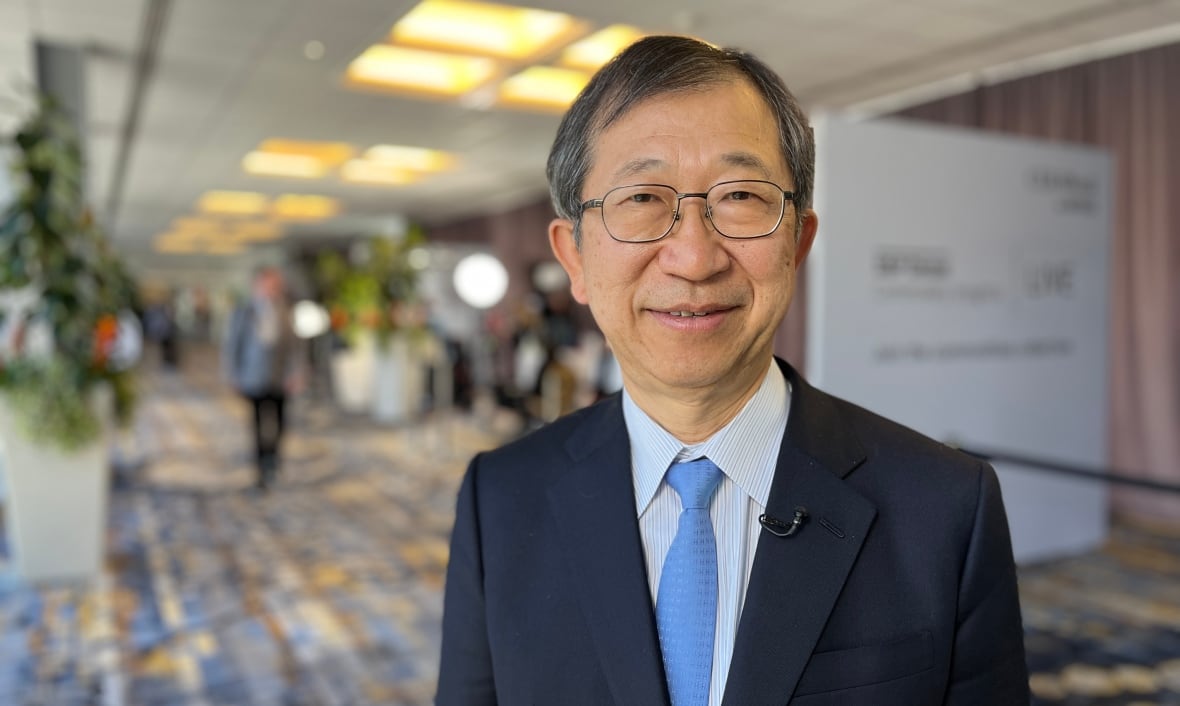 A man in a navy suit and a light blue tie poses for a photo at a hotel conference centre.